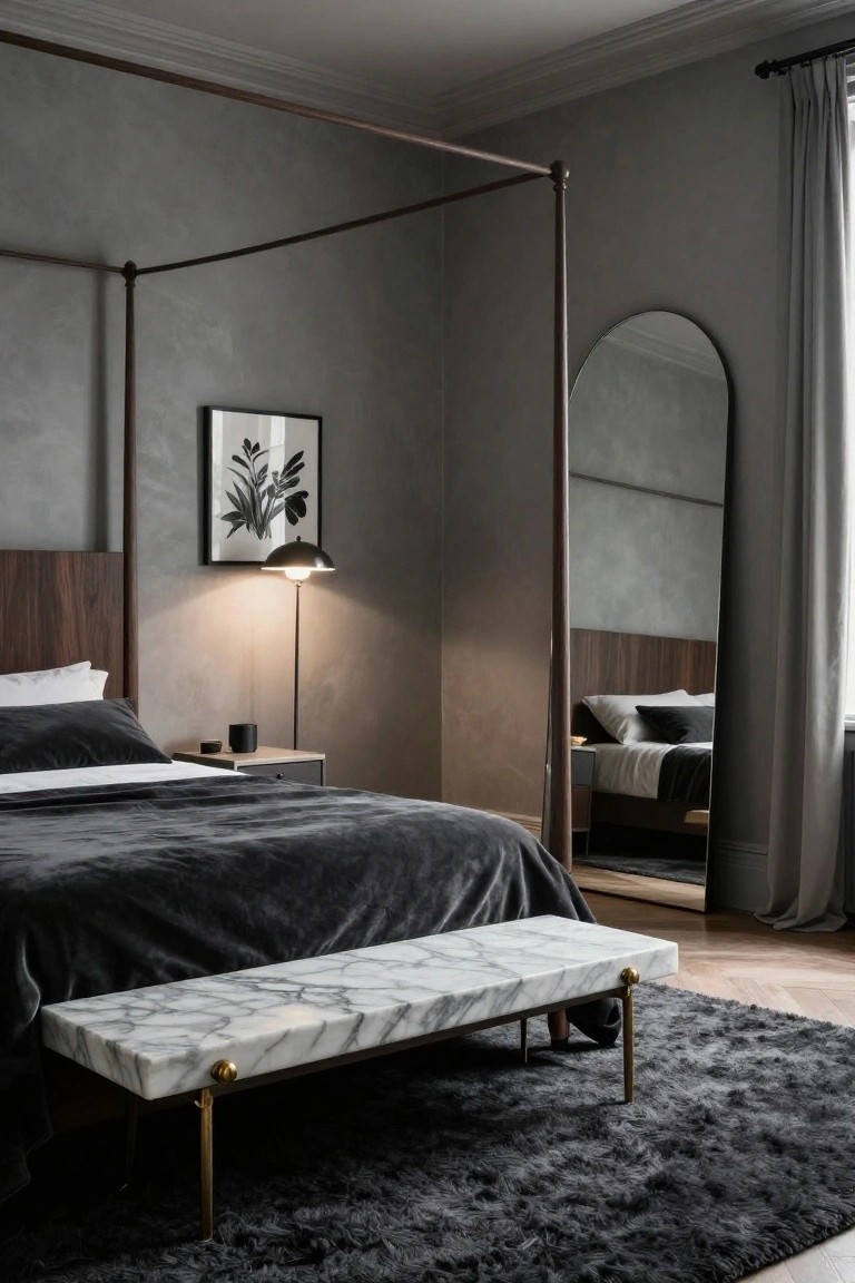 A grey-toned bedroom with a dark wood four-poster bed covered in plush grey velvet bedding, a white marble bench on brass legs at the foot of the bed, an arched floor mirror, a bedside lamp, and a black shag rug on wood floors.