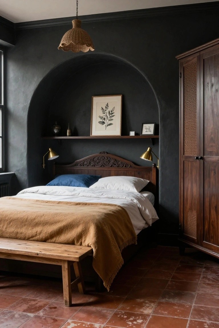 Bedroom with dark charcoal curved wall arch recess containing framed leaf artwork and shelf above wooden carved headboard bed with blue pillows, white sheets, tan throw blanket, wooden bench at foot, and tall wardrobe with rattan panels on terracotta tile floor.