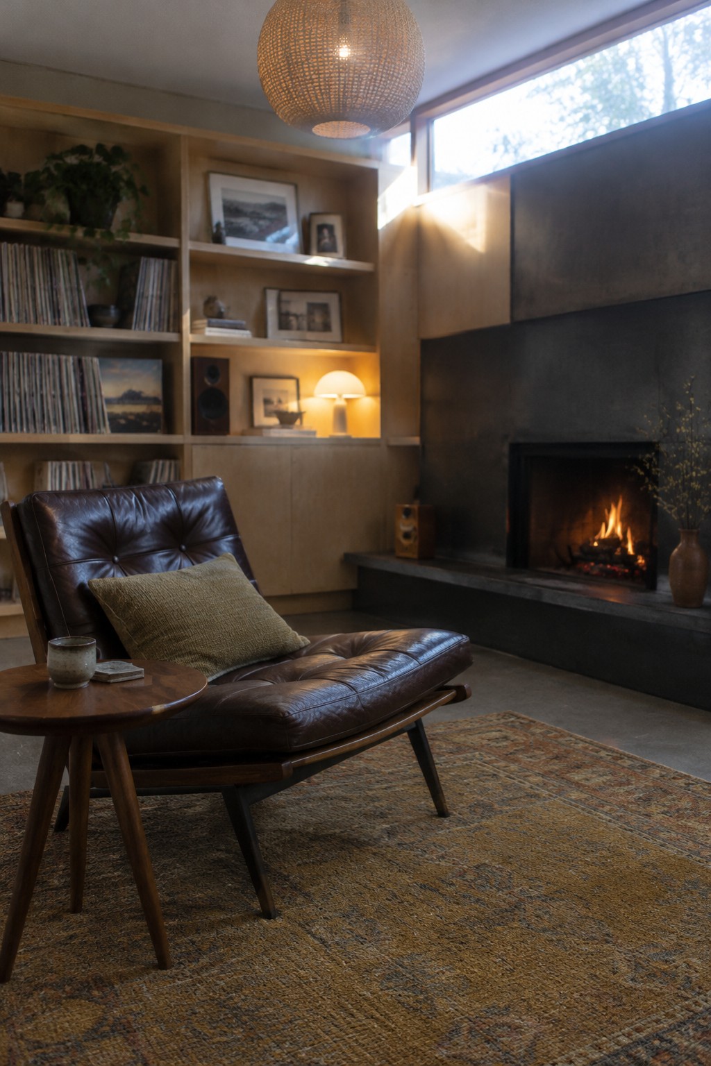 A dark brown leather lounge chair sits on a patterned rug beside a round wooden table in a living room with built-in shelves and a fireplace.